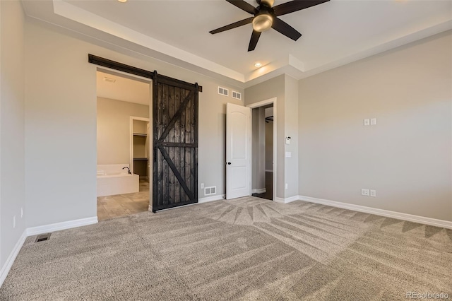 unfurnished bedroom featuring carpet floors, a barn door, a walk in closet, and baseboards