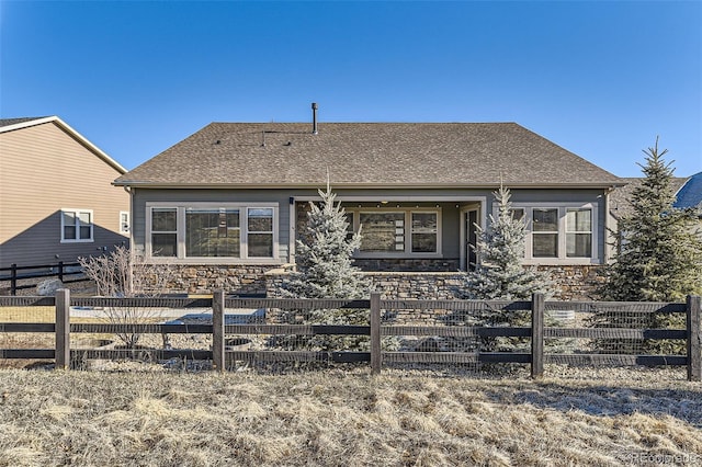 view of front of home with stone siding, a shingled roof, and fence