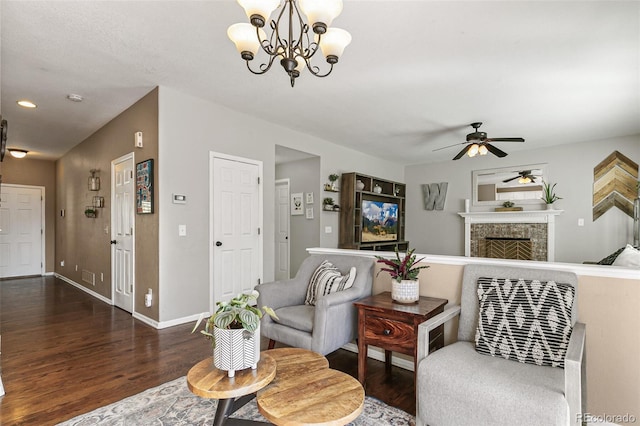 living area with a fireplace, ceiling fan with notable chandelier, baseboards, and dark wood finished floors
