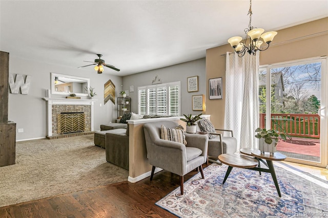 living room with a fireplace with raised hearth, ceiling fan with notable chandelier, baseboards, and wood finished floors