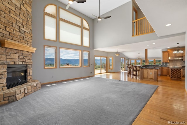 1680 Elk View Rd, Larkspur, CO 80118 - unfurnished living room featuring ceiling fan, a fireplace, light wood finished floors, and a towering ceiling