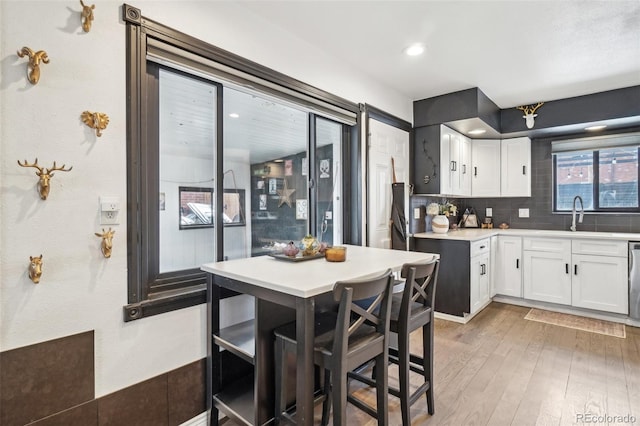 kitchen with white cabinets, a sink, light countertops, light wood-style floors, and decorative backsplash