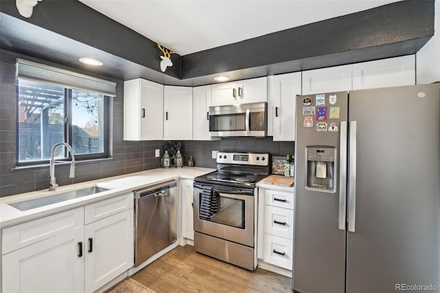 kitchen with light wood-type flooring, light countertops, a sink, stainless steel appliances, and decorative backsplash