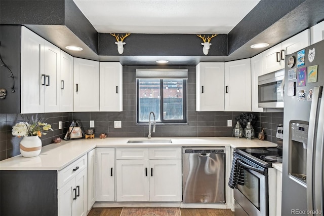 kitchen featuring light countertops, backsplash, white cabinets, stainless steel appliances, and a sink