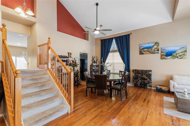 dining area featuring baseboards, wood finished floors, stairs, high vaulted ceiling, and ceiling fan with notable chandelier