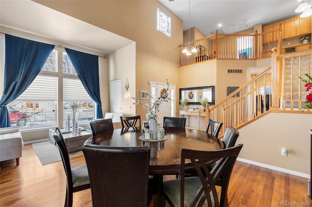 dining space with light wood finished floors, visible vents, a towering ceiling, stairway, and baseboards