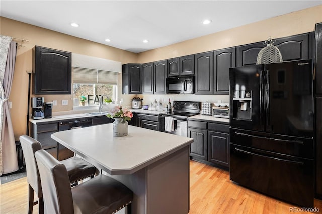 kitchen with a breakfast bar area, light wood-style flooring, dark cabinets, a center island, and black appliances