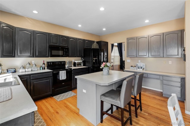 kitchen with a breakfast bar, a center island, built in desk, light countertops, and black appliances