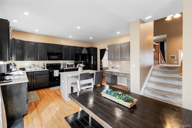 kitchen featuring light wood finished floors, light countertops, a kitchen island, a sink, and black appliances