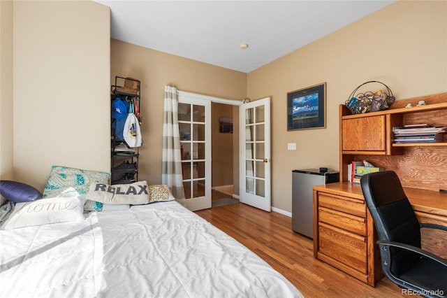 bedroom featuring french doors, light wood-type flooring, freestanding refrigerator, and baseboards