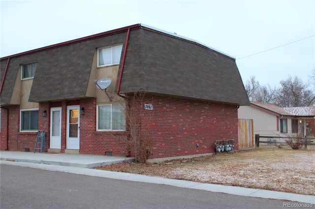 view of property exterior featuring a shingled roof, mansard roof, and brick siding