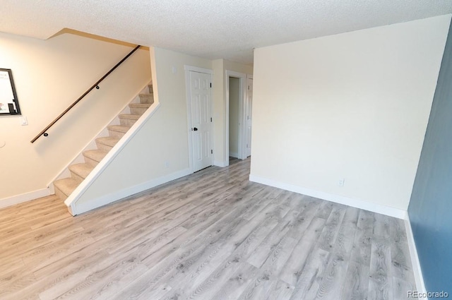 unfurnished room with stairs, a textured ceiling, baseboards, and wood finished floors