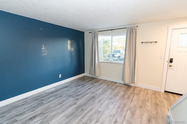 empty room with a textured ceiling, light wood-type flooring, visible vents, and baseboards