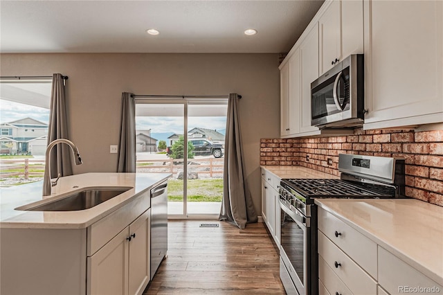 kitchen featuring appliances with stainless steel finishes, sink, white cabinets, decorative backsplash, and light hardwood / wood-style flooring