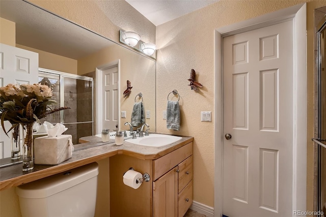 bathroom featuring a textured ceiling, vanity, an enclosed shower, and toilet