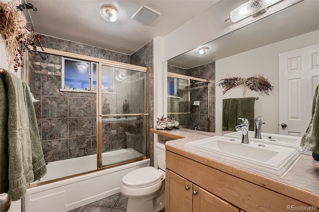 full bathroom featuring vanity, shower / bath combination with glass door, tile patterned floors, toilet, and a textured ceiling