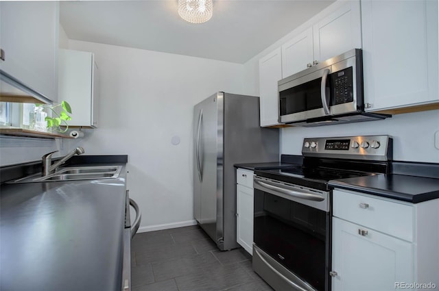 kitchen featuring appliances with stainless steel finishes, dark countertops, a sink, and white cabinetry