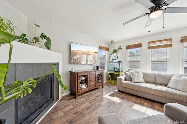 living area featuring a glass covered fireplace, a ceiling fan, baseboards, and wood finished floors