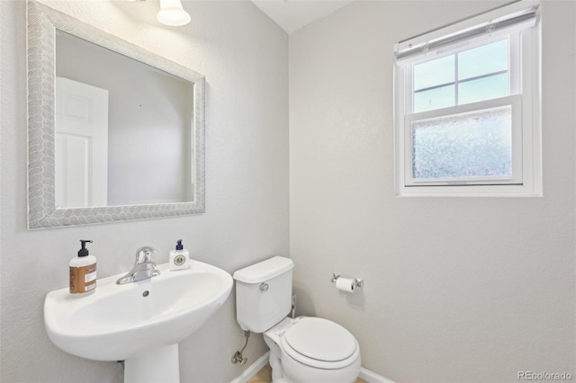 half bathroom with toilet, baseboards, and a sink