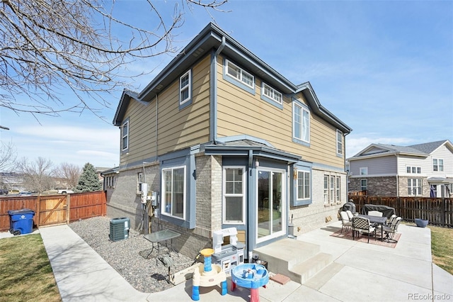 rear view of property featuring brick siding, central AC unit, a fenced backyard, and a patio area