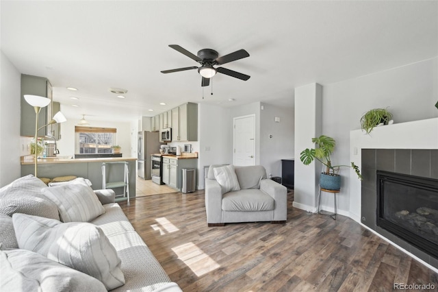 living area with light wood finished floors, baseboards, recessed lighting, a fireplace, and a ceiling fan