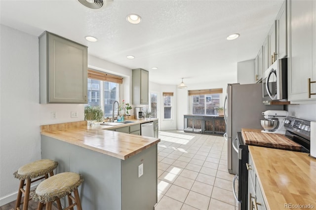 kitchen with butcher block countertops, a kitchen bar, light tile patterned flooring, stainless steel appliances, and a sink