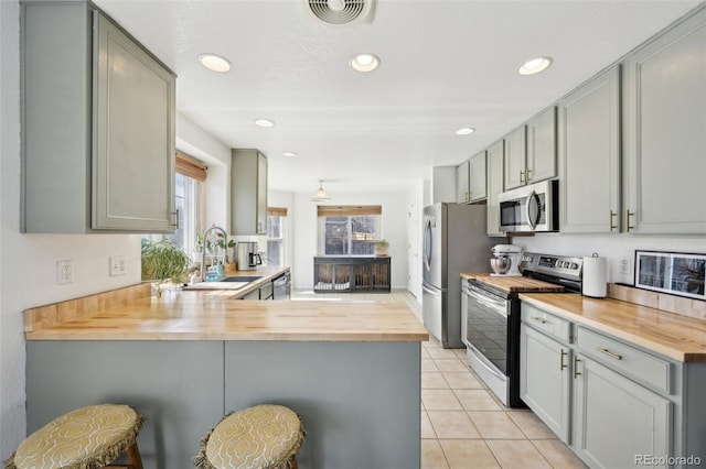 kitchen with visible vents, a peninsula, gray cabinetry, butcher block countertops, and appliances with stainless steel finishes