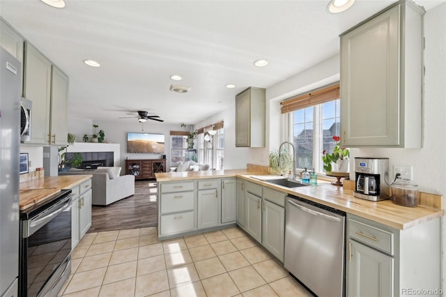 kitchen featuring wooden counters, gray cabinetry, a tiled fireplace, stainless steel appliances, and a sink