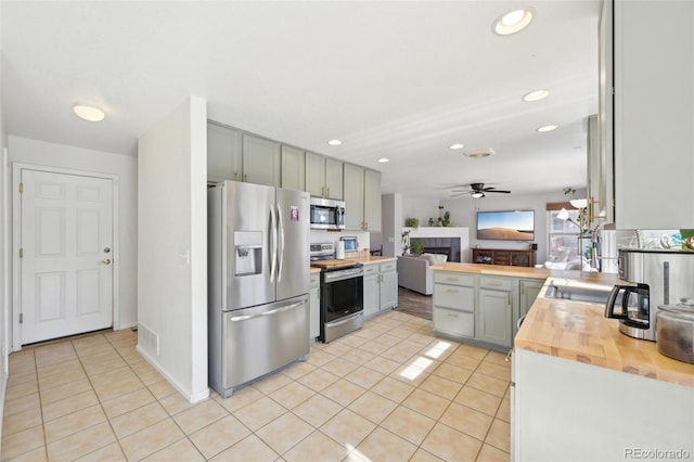 kitchen with light tile patterned flooring, a ceiling fan, appliances with stainless steel finishes, and wood counters