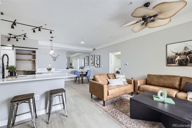 living room featuring washer / clothes dryer, rail lighting, light wood-style flooring, a ceiling fan, and a textured ceiling