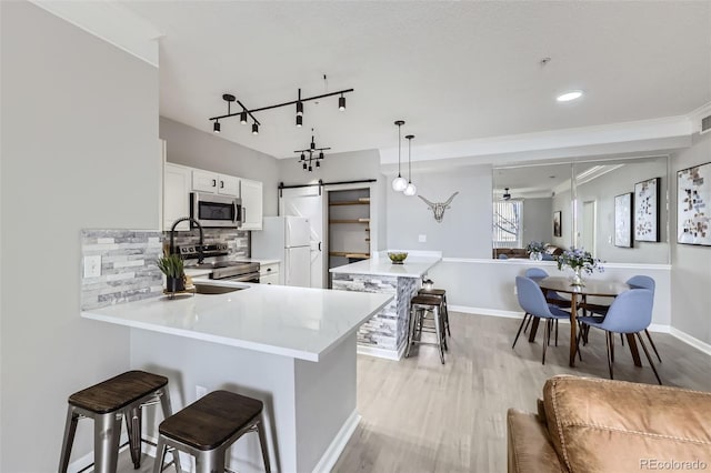 kitchen with a barn door, white cabinets, a peninsula, stainless steel appliances, and a kitchen bar