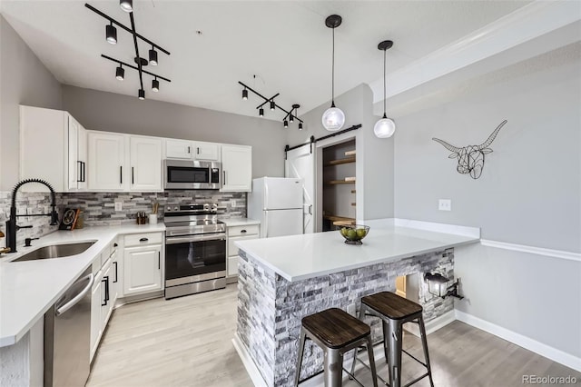 kitchen featuring a barn door, white cabinets, appliances with stainless steel finishes, light countertops, and a sink