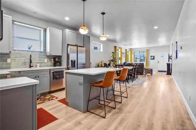 kitchen featuring a breakfast bar, sink, gray cabinetry, hanging light fixtures, and stainless steel appliances