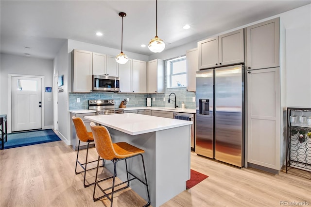 kitchen with sink, stainless steel appliances, a center island, light hardwood / wood-style floors, and decorative light fixtures