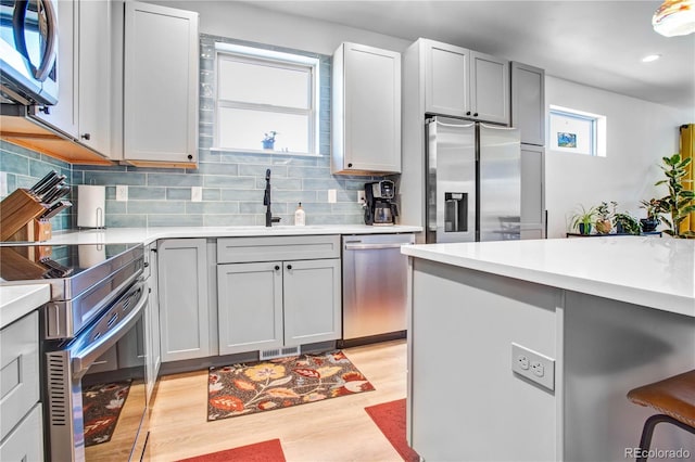 kitchen featuring sink, gray cabinets, backsplash, stainless steel appliances, and light hardwood / wood-style floors