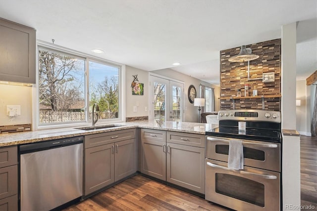 kitchen with gray cabinets, dark wood-style flooring, appliances with stainless steel finishes, light stone countertops, and a sink