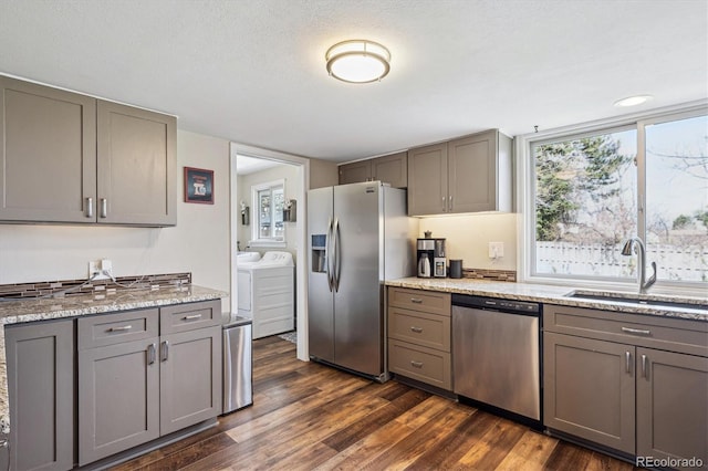 kitchen featuring gray cabinets, appliances with stainless steel finishes, a sink, dark wood-style floors, and washer and clothes dryer