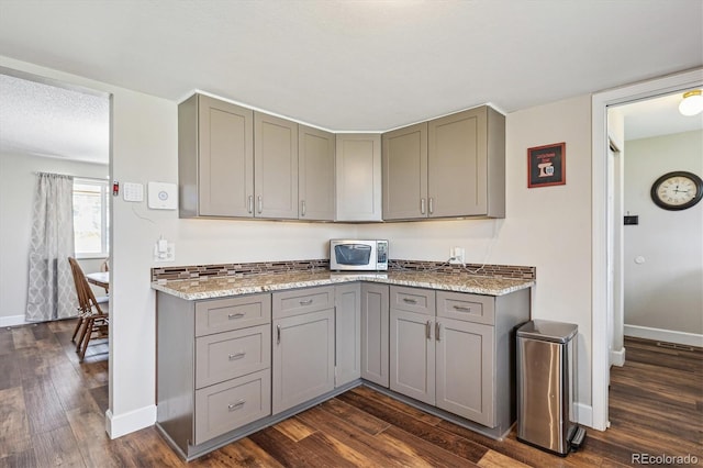 kitchen featuring baseboards, dark wood-style floors, gray cabinetry, and light stone countertops