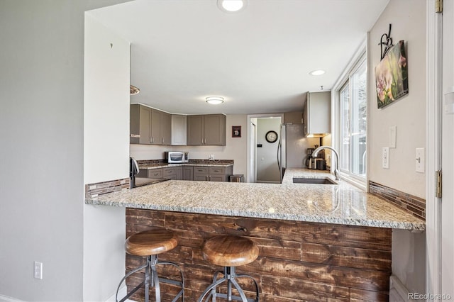 kitchen with a peninsula, light stone countertops, a sink, gray cabinetry, and stainless steel appliances