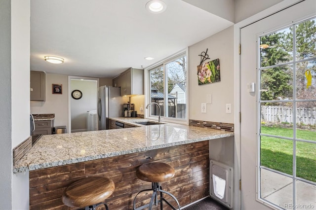 kitchen with freestanding refrigerator, light stone counters, a wealth of natural light, and a sink