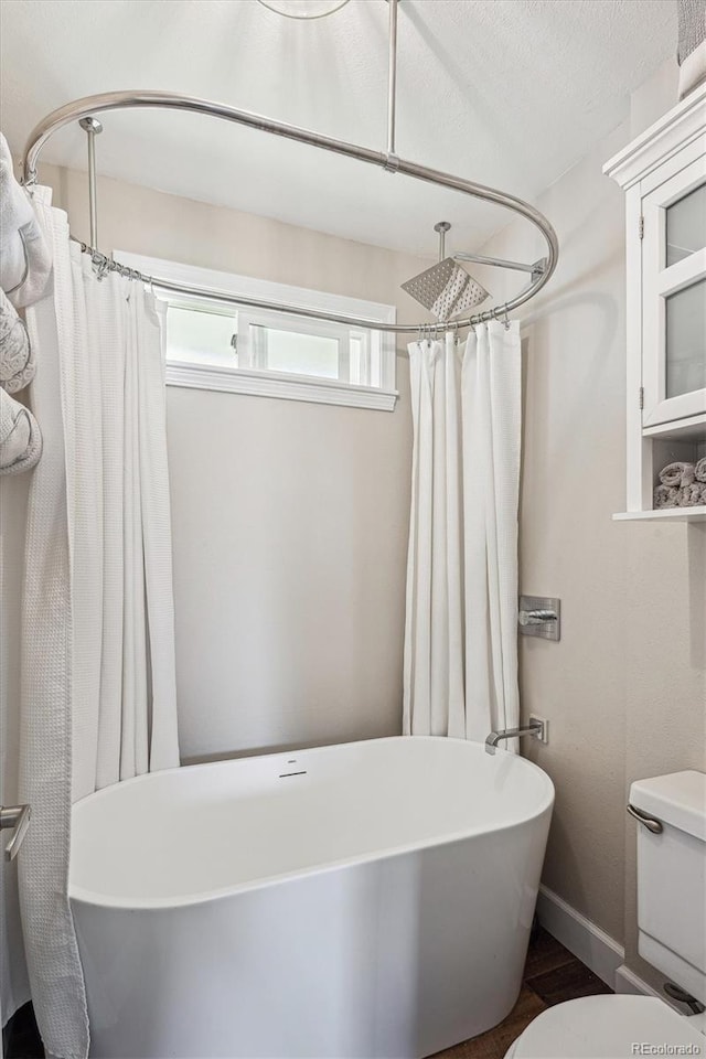 bathroom with toilet, a freestanding bath, curtained shower, and wood finished floors