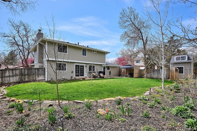 rear view of house with a gazebo, a fenced backyard, a chimney, a patio, and a yard