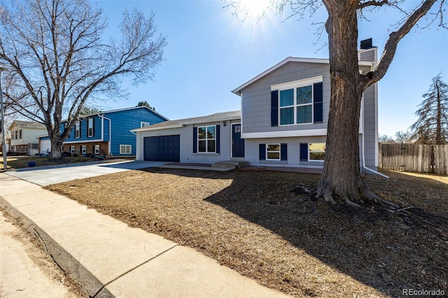 tri-level home featuring an attached garage, brick siding, fence, concrete driveway, and a chimney