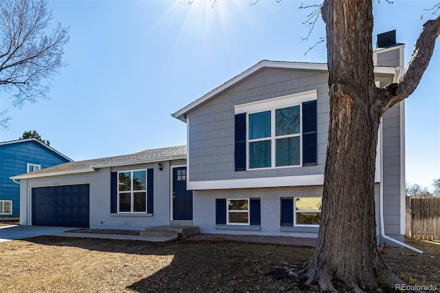 split level home featuring concrete driveway, brick siding, an attached garage, and fence