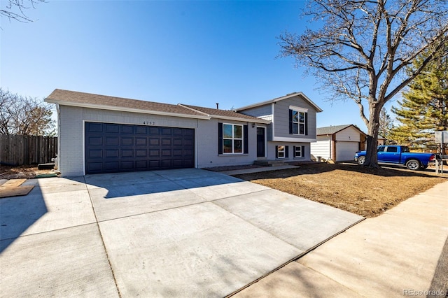 split level home featuring a garage, driveway, brick siding, and fence