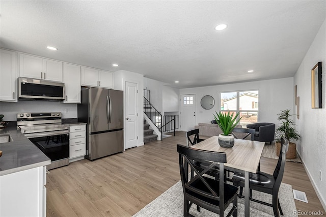 kitchen featuring white cabinets, dark countertops, stainless steel appliances, a textured ceiling, and light wood-style floors