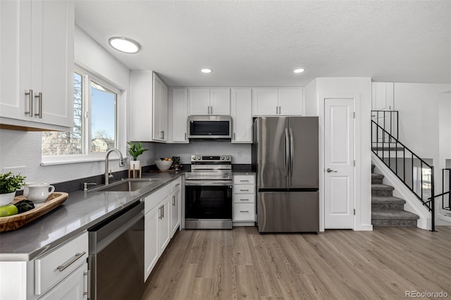 kitchen featuring a textured ceiling, light wood-style flooring, a sink, white cabinets, and appliances with stainless steel finishes