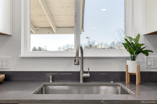 interior details with a textured wall, stainless steel countertops, a sink, and white cabinets