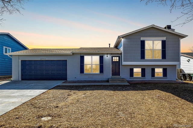 tri-level home featuring an attached garage, driveway, and brick siding