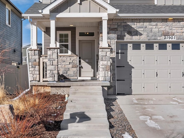 21901 E 42nd Pl, Aurora, CO 80019 - doorway to property with stone siding, board and batten siding, concrete driveway, a shingled roof, and a porch